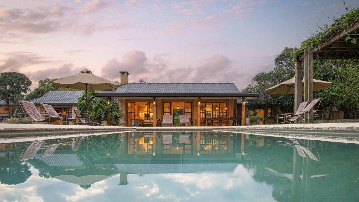 Reflection of Amani House and sunset clouds in a still swimming pool with lounge chairs on the deck.