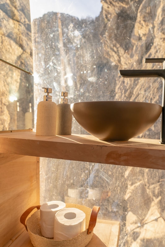 A view of a sink in a transparent pod mounted to a cliff face.