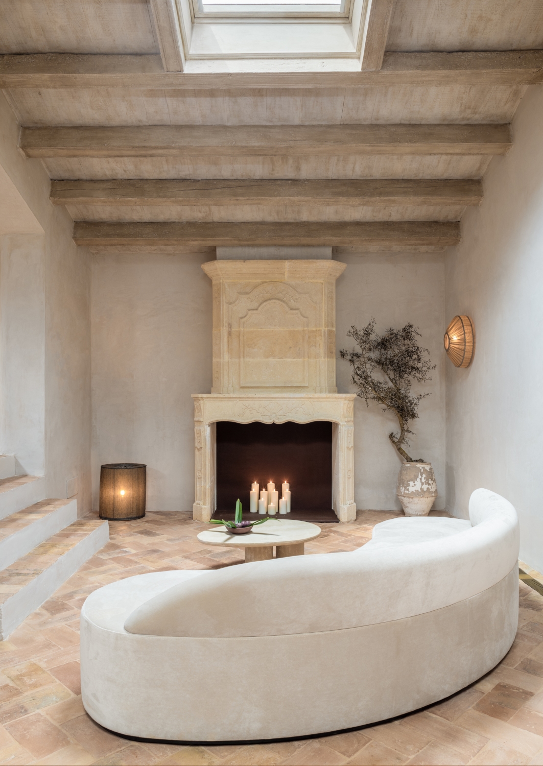 Intimate lounge at Son Vell in Balearic Islands Spain with a curved white sofa and candles in a stone fireplace.