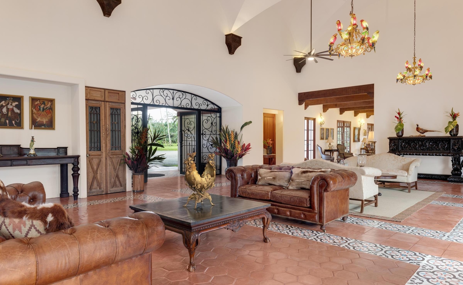 Spacious luxury lobby with leather Chesterfield sofas, tiled floors, and colorful bird chandeliers hanging from high ceilings.