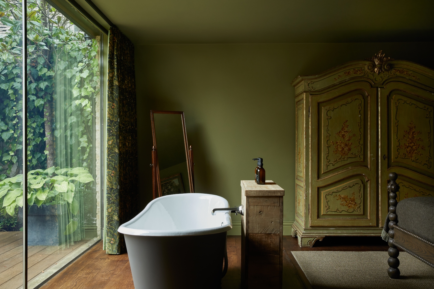 Interior of a room with green walls and in the centre is a freestanding bathtub next to a large window.