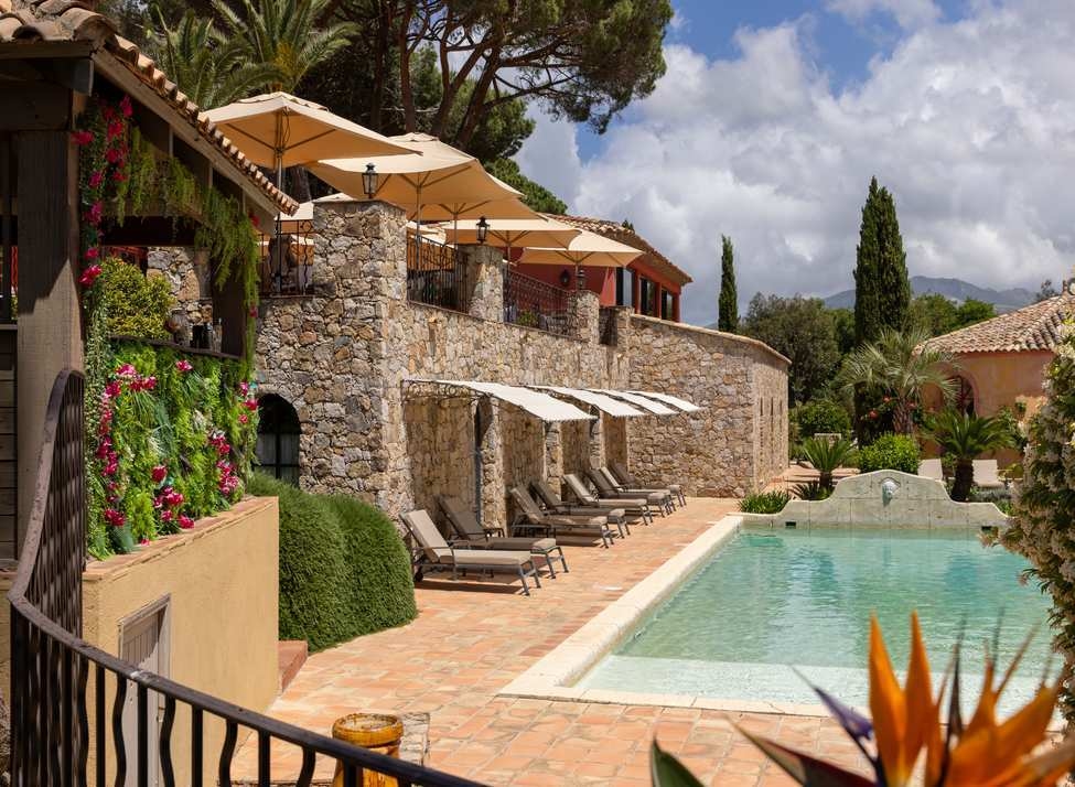 Wide view of a swimming pool and a stone building with trees and mountains in the background