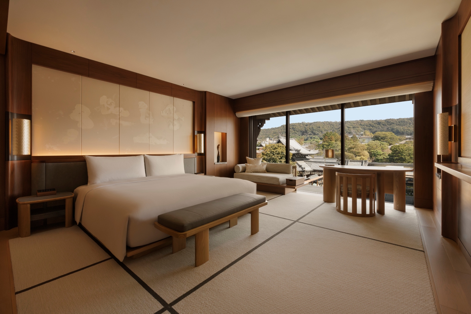 Interior bedroom with neutral-toned bedding and soft lighting with a wall of windows overlooking a temple and greenery.