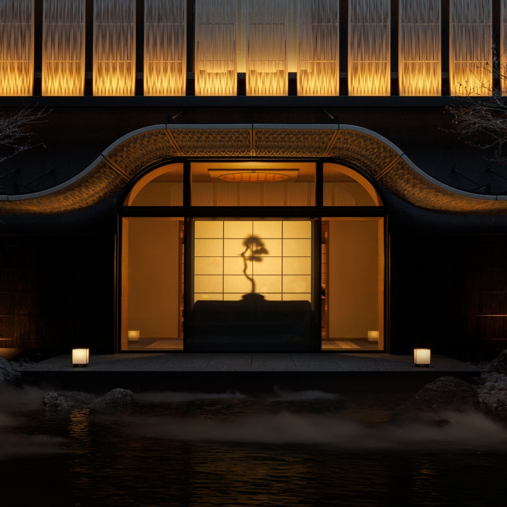 Exterior view of the hotel at night lit from within showing a Japanese screen wall with a bonsai plant illuminated.