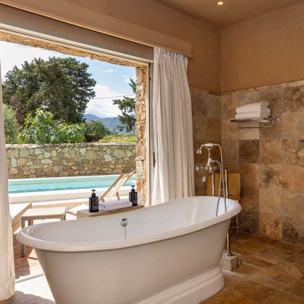 A freestanding bathtub beside sliding doors open to an outdoor pool and terrace