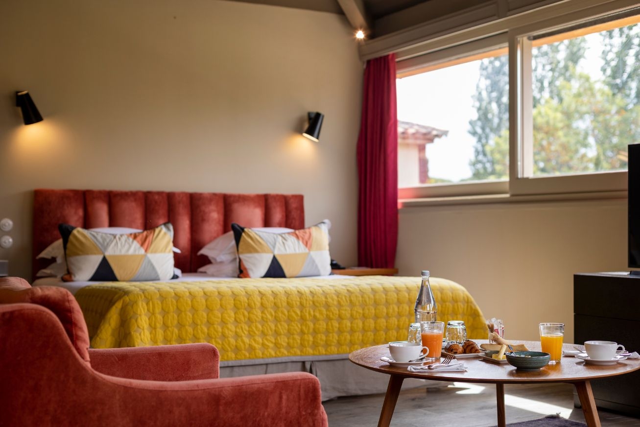 A hotel room with a yellow and red bed and a coffee table set for breakfast