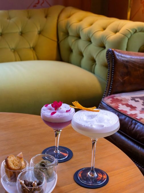 Close-up of two cocktails and snacks on a table beside a green couch
