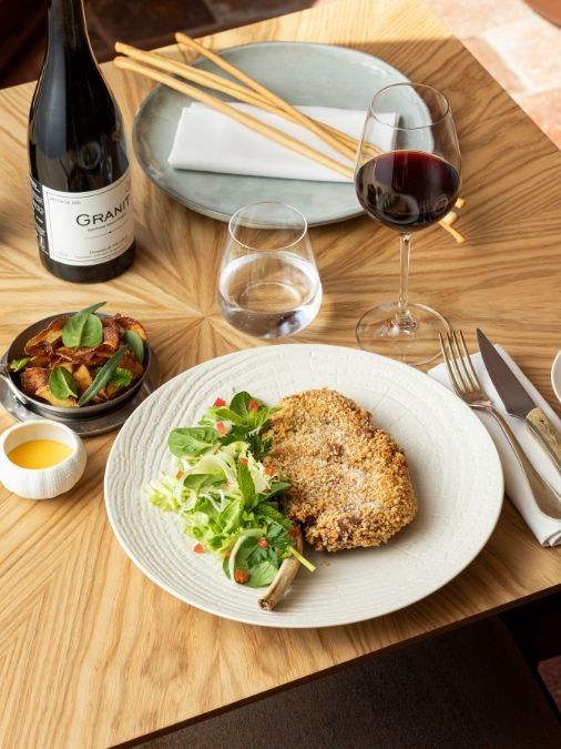 Close-up of a plate of breaded meat and salad beside a bottle and glass of red wine
