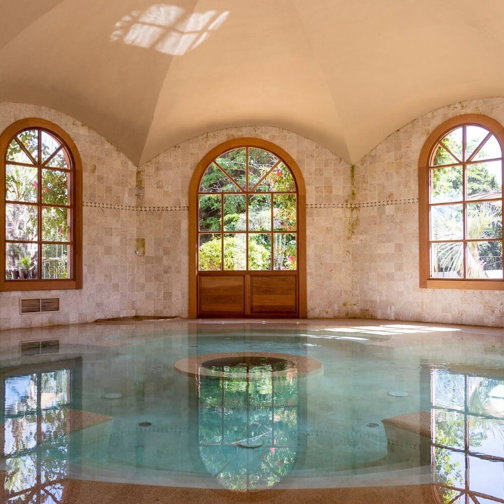 An indoor pool beneath a vaulted ceiling with three arched windows around it