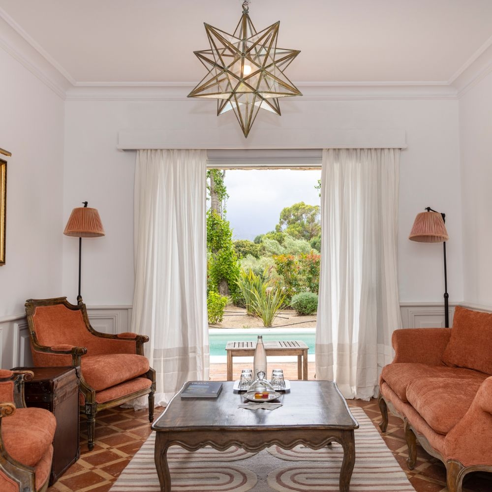 A living area with orange upholstered furniture and sliding doors leading to a pool and garden