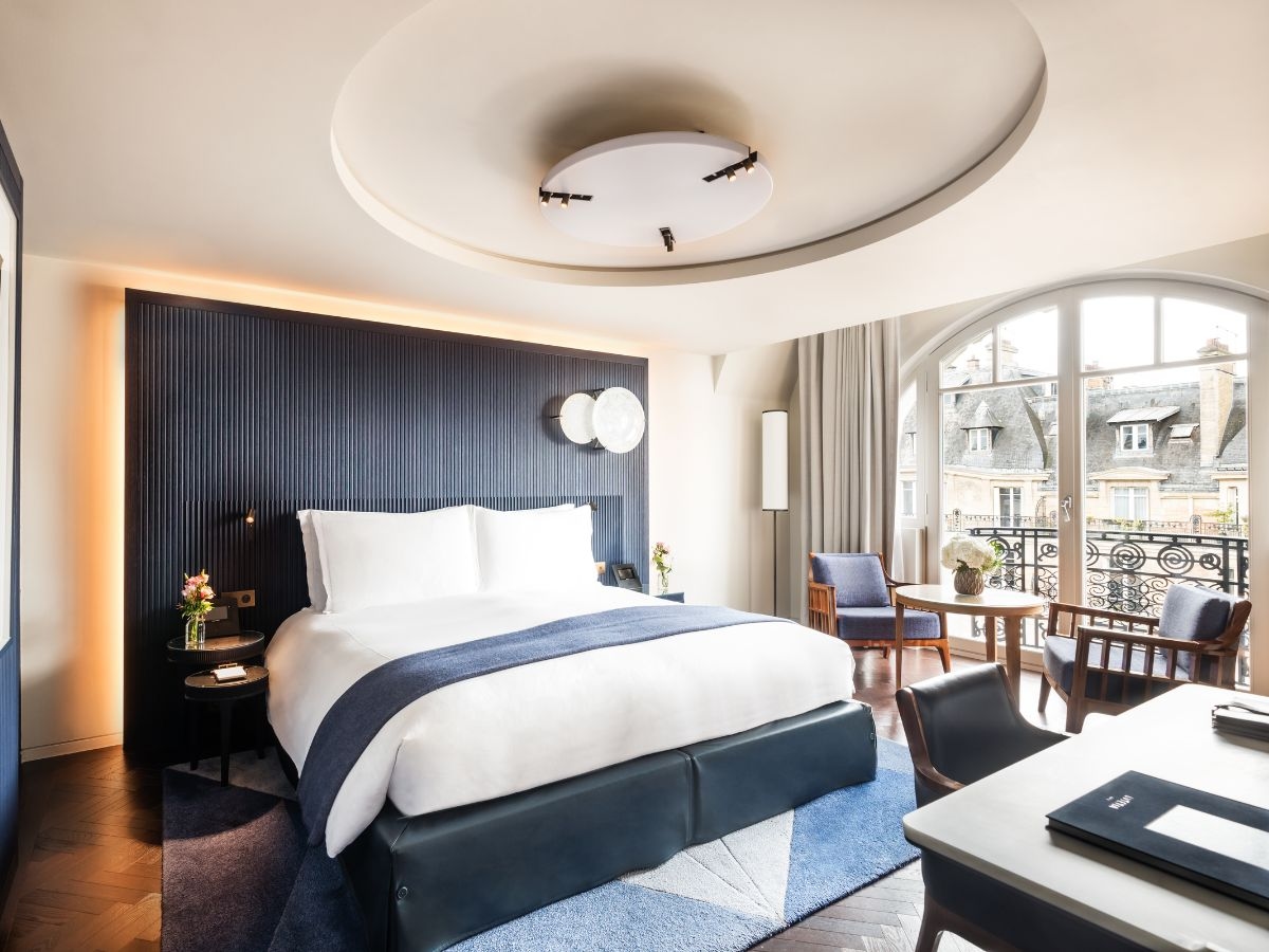 A hotel guest room with a bed, arched window and sitting area