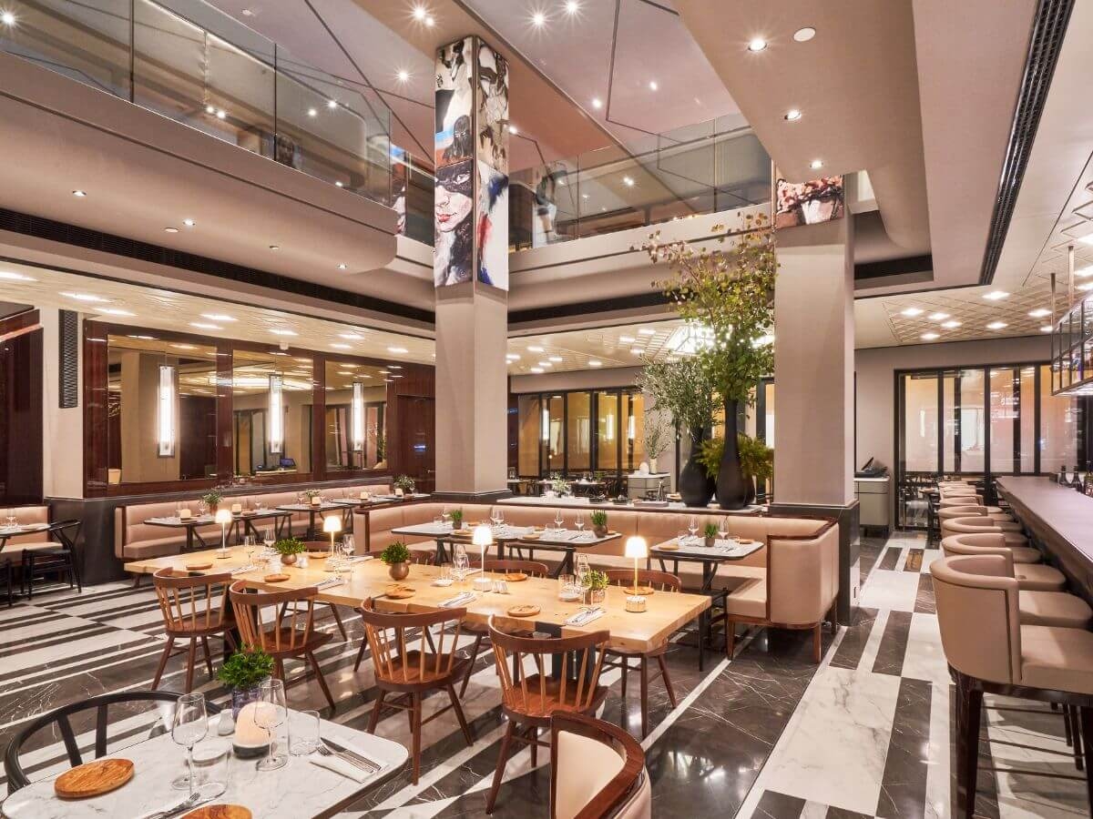 A restaurant with several tables, tiled floors and high ceilings