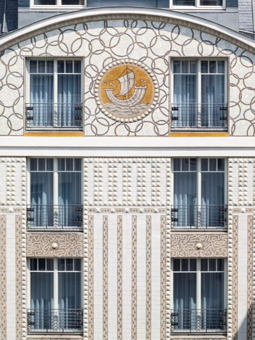 A white building facade with mosaic patterns and an image of a ship at sea