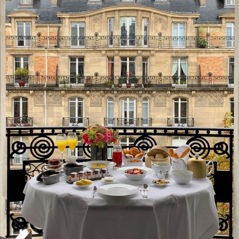 A round table set for breakfast on a balcony facing an ornate building