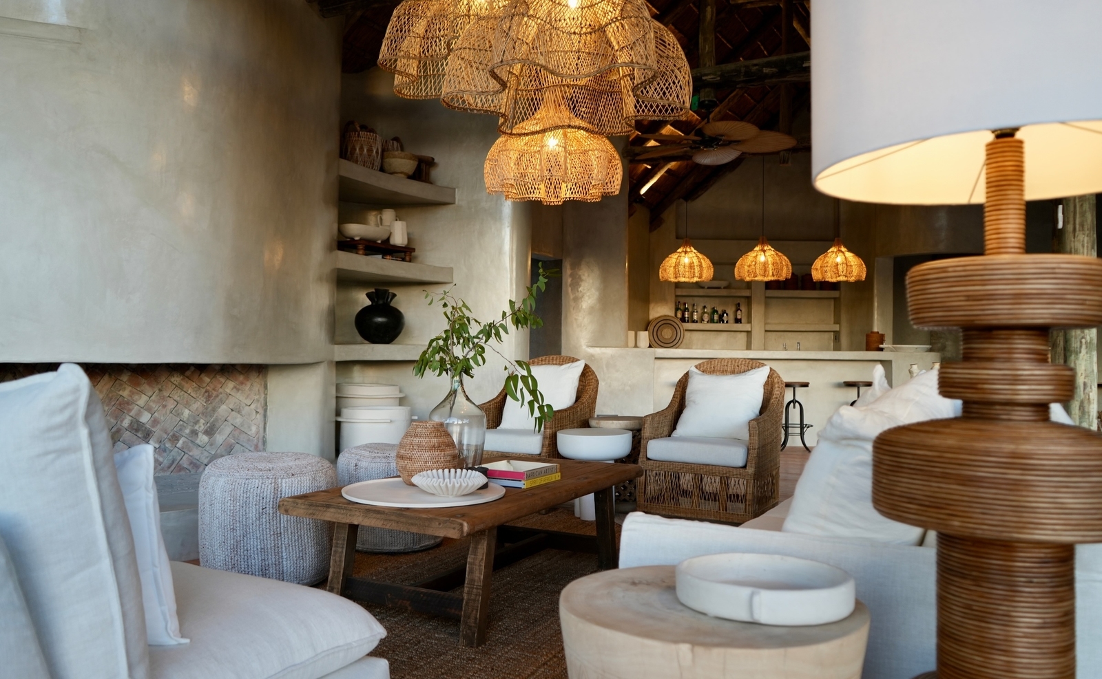A decorated lounge area at a safari lodge with white sofas, woven chairs, and large woven chandeliers.