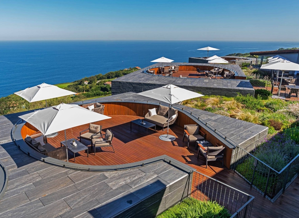Outdoor terraces at with white umbrellas overlooking a vast blue sea.
