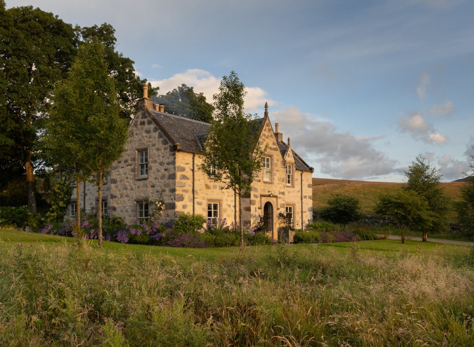 Stone farmhouse in mid distance with green meadow in the foreground and Scottish fells and blue sky beyond.