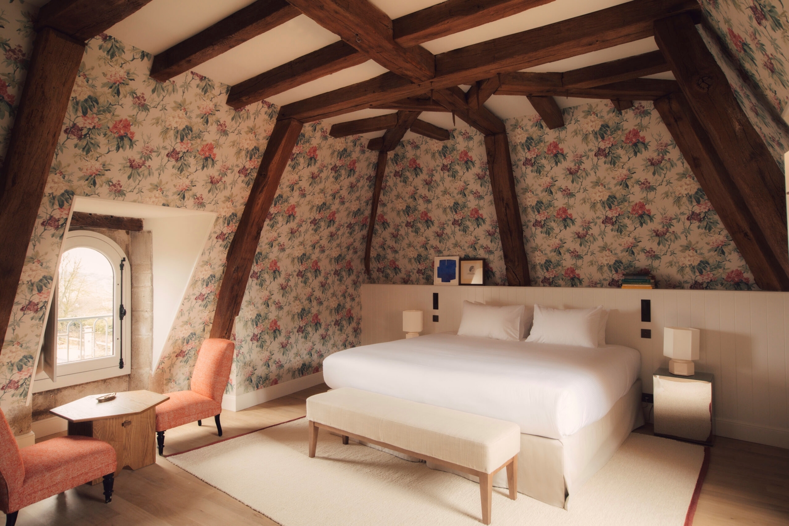 Bedroom with a bed with white bedding, floral wallpaper and dark wood beams.