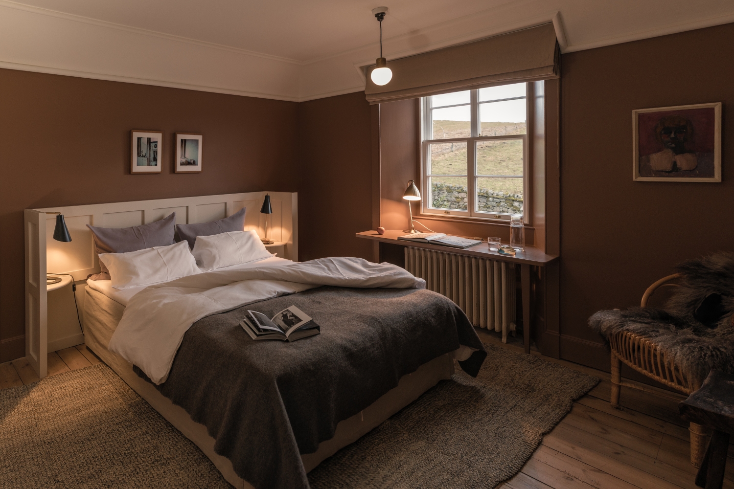 Bedroom with a bed with white and grey bedding and brown walls, and a window overlooking the Scottish Highland mountains.