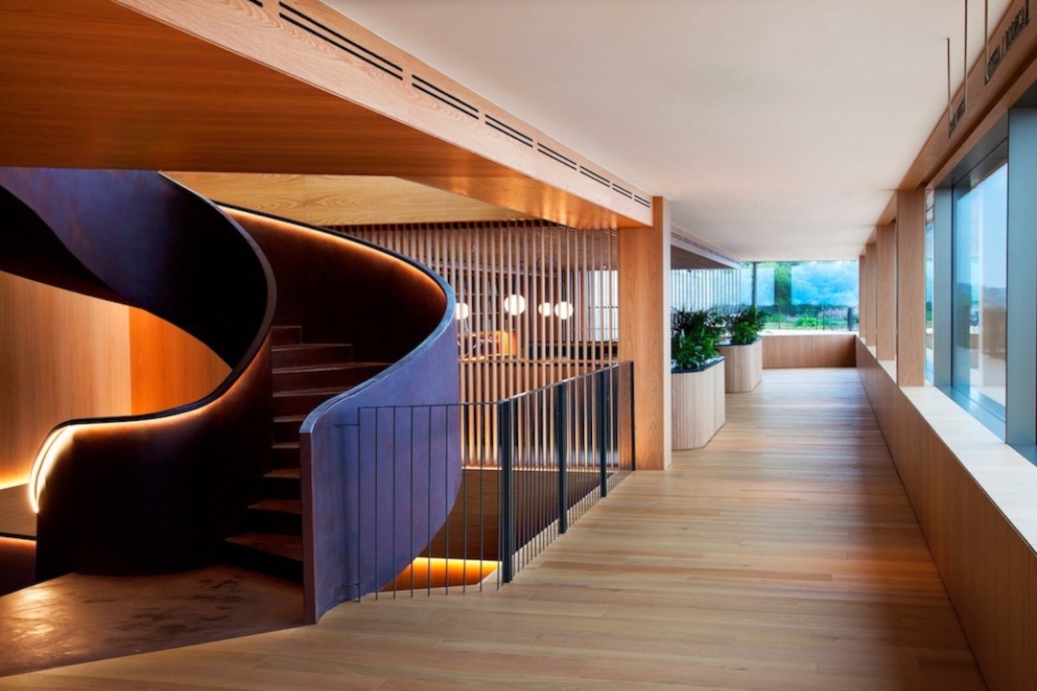 Interior of a lobby area with a curving dark staircase and light wood floors.