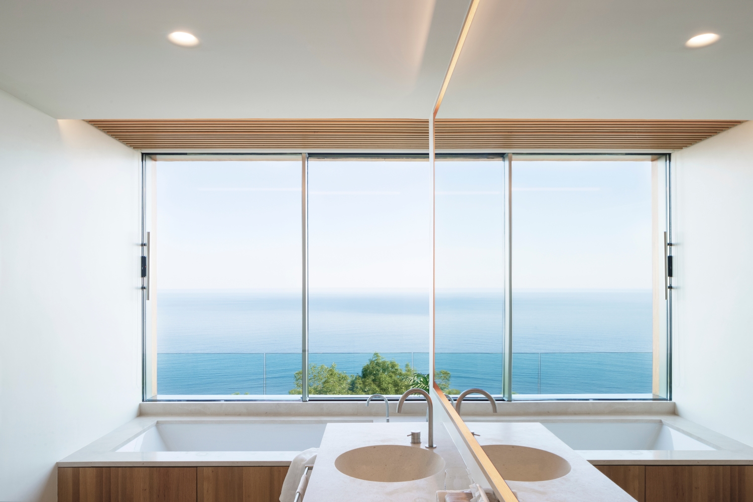Interior of a minimalist bathroom with a single sink and bathtub and huge window overlooking the sea.