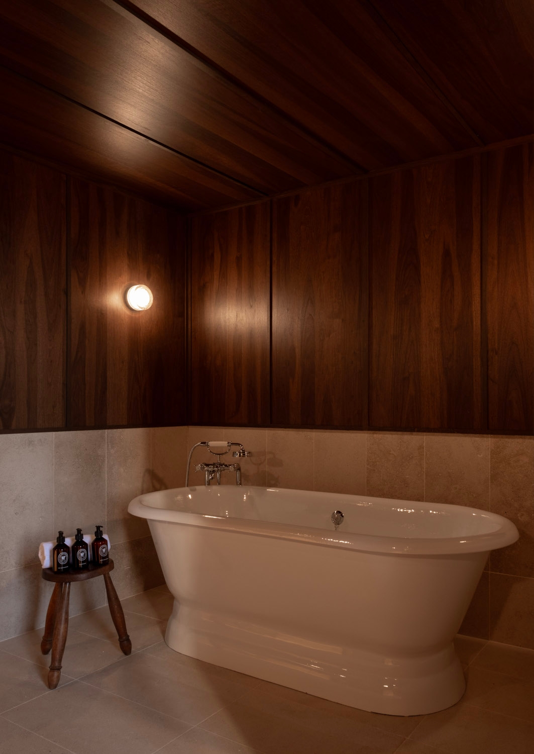 Interior of a bathroom with a standalone white bathtub and dark wood walls.