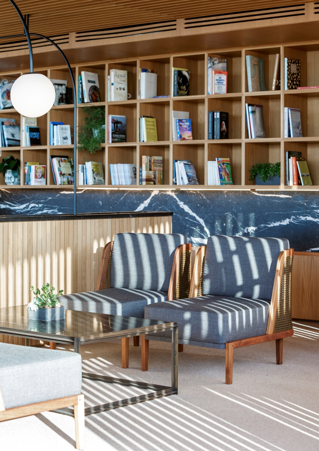 Interior of a sunny sitting area with shelves full of books and several lounge chairs.