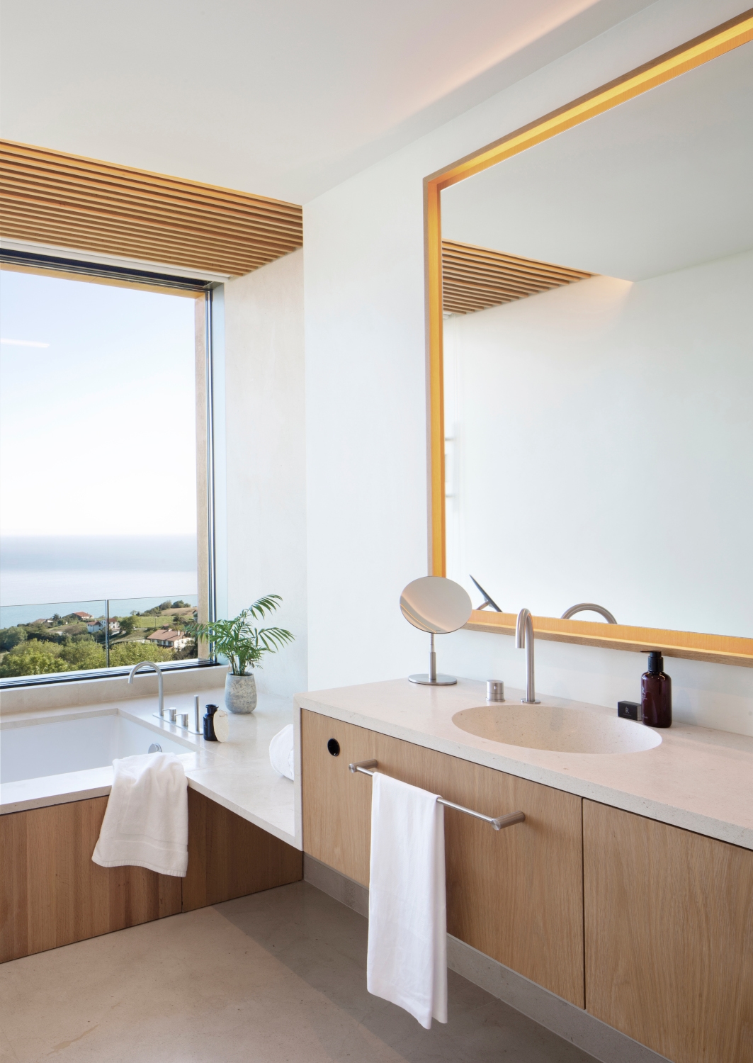 Interior of a minimalist bathroom with a single sink and bathtub and huge window overlooking the sea.