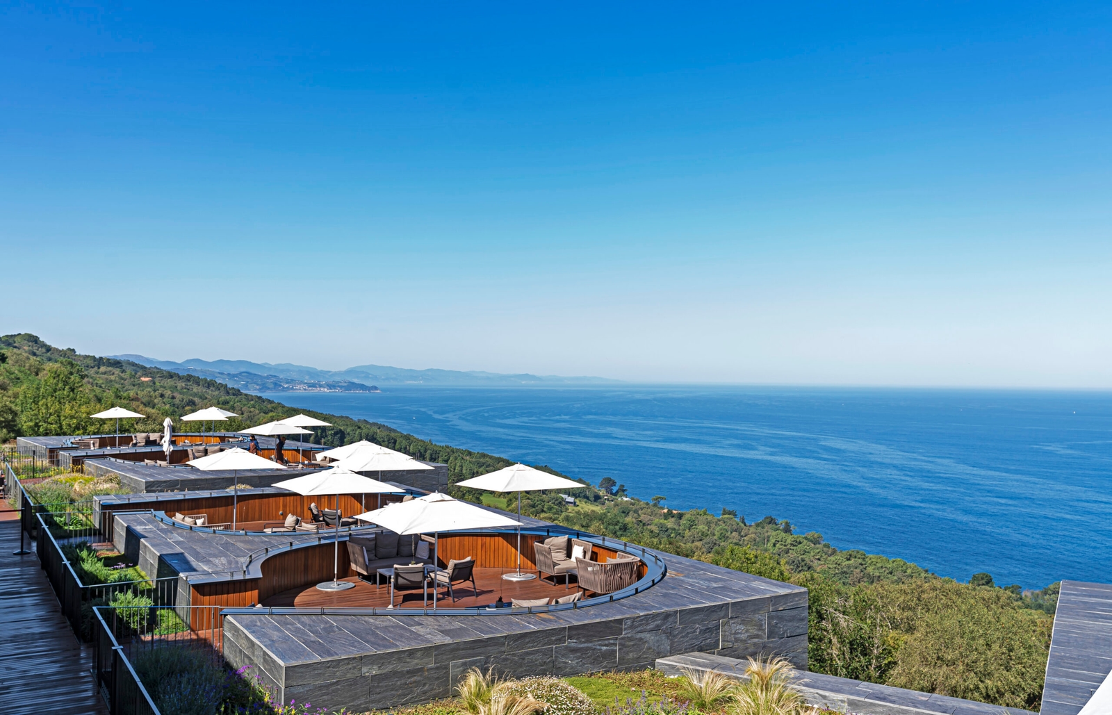 Outdoor terraces at with white umbrellas overlooking a vast blue sea.