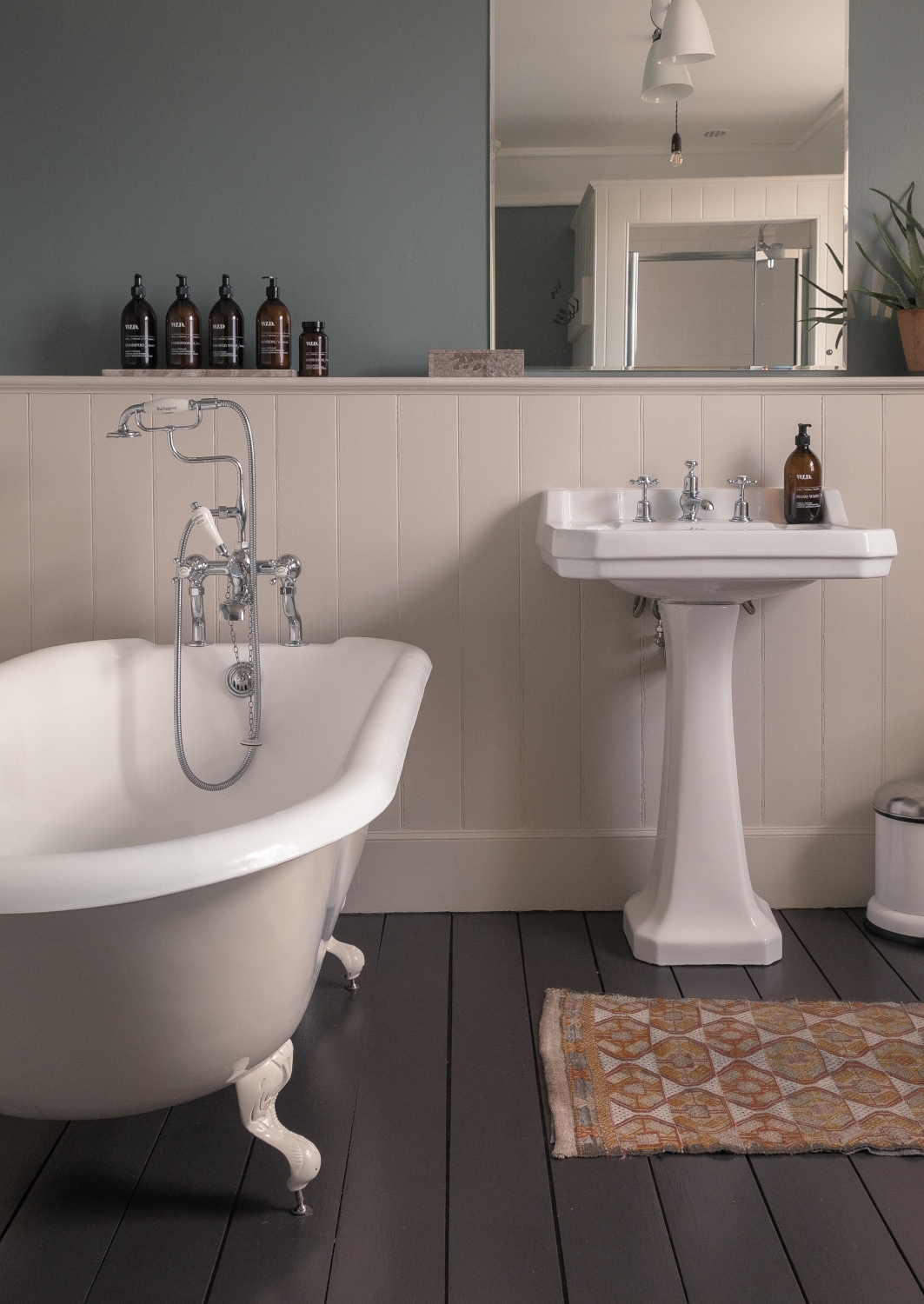 A bathroom with a standalone bathtub and historic sink and wooden floors.