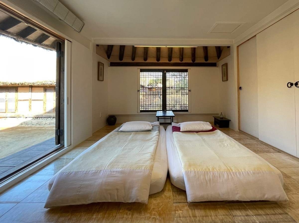Traditional Korean hanok bedroom featuring two floor mattresses side-by-side at Rakkojae Andong, with open sliding doors leading to an outdoor courtyard.
