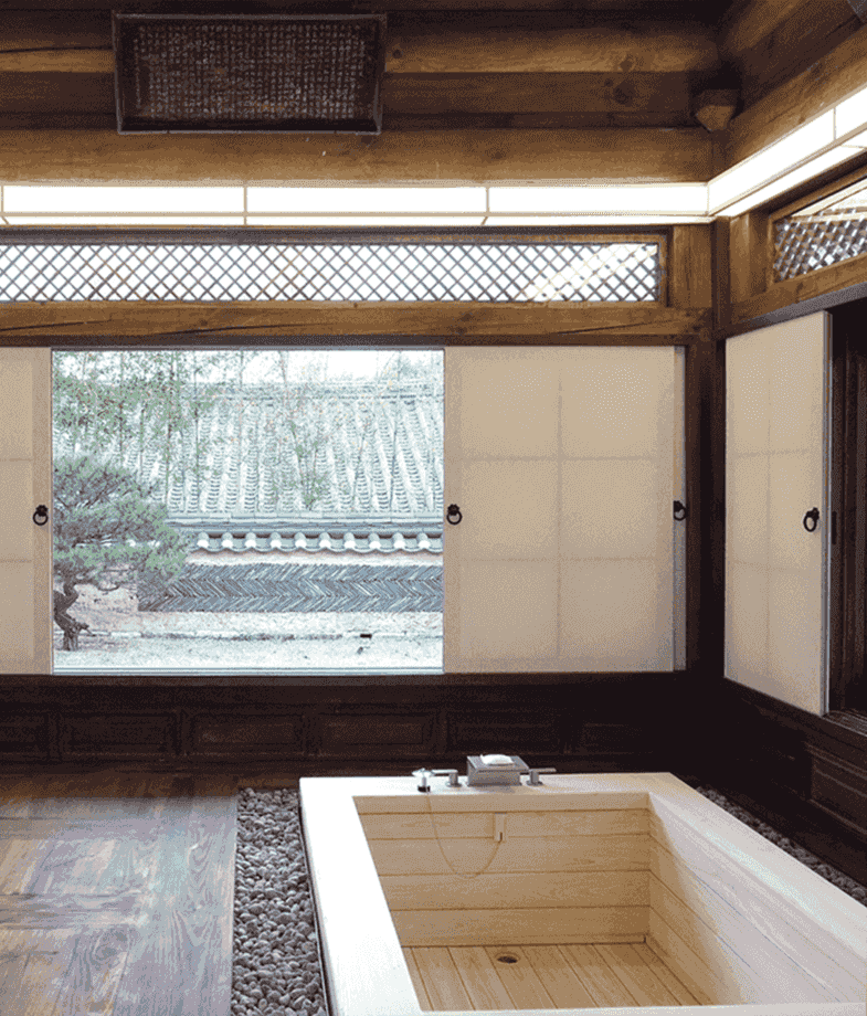 Luxury wooden bathtub inside a traditional Korean hanok bathroom at Rakkojae Andong Hahoe, with view of a courtyard.