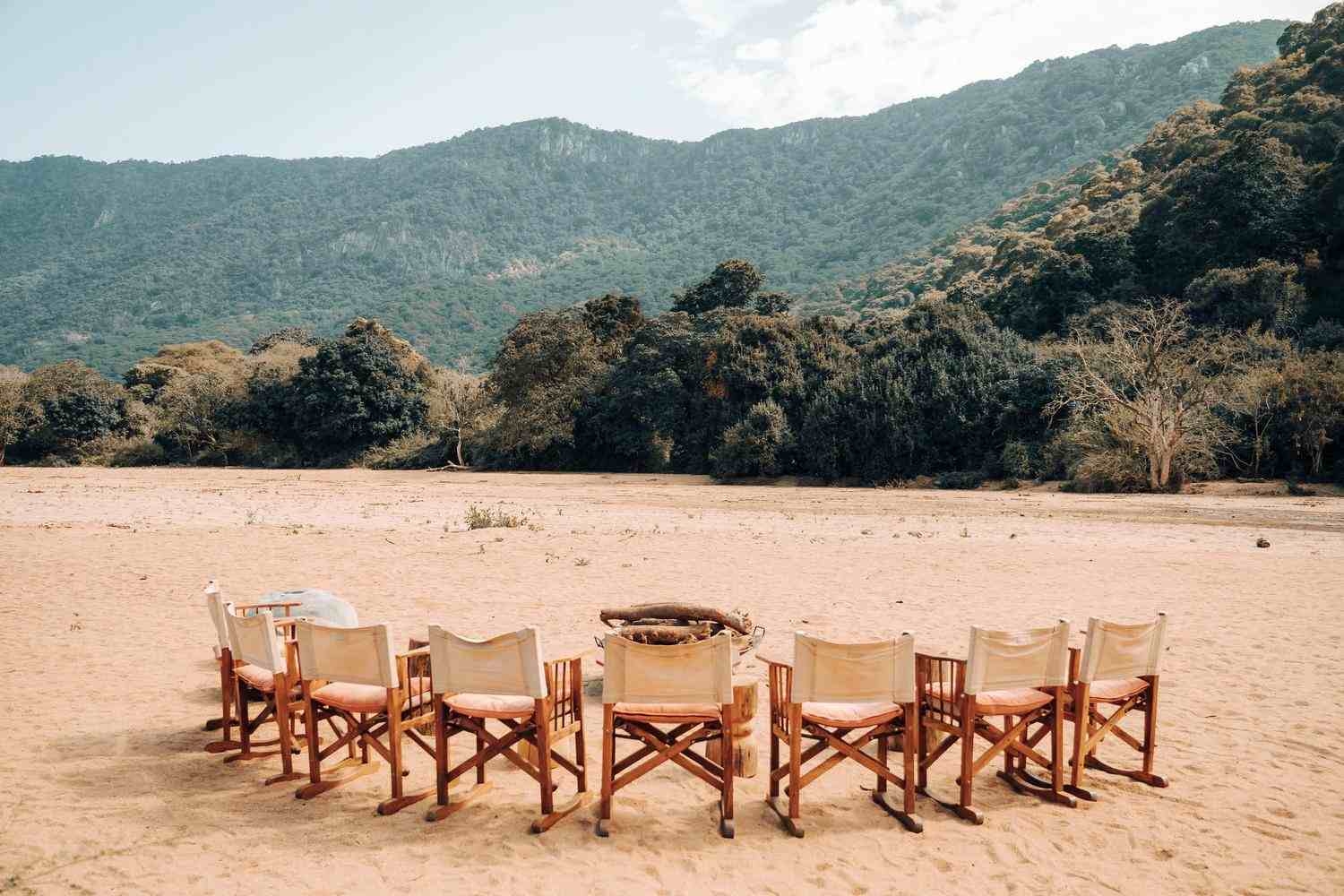 A semi-circle of wooden and canvas chairs is arranged around a firepit, with views of the savannah, forest and rift valley escarpment beyond.