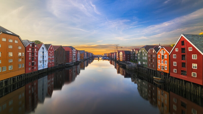 Brightly colored wooden buildings lining both sides of a still river reflecting a soft sunset sky.