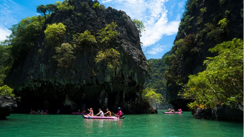 People paddling pink canoes through emerald water by limestone cliffs during luxury asian family trips.