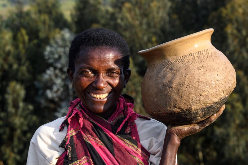Smiling woman in a pink and black scarf holding a piece of unglazed terracotta pottery. Find culture on luxury Rwanda vacations.
