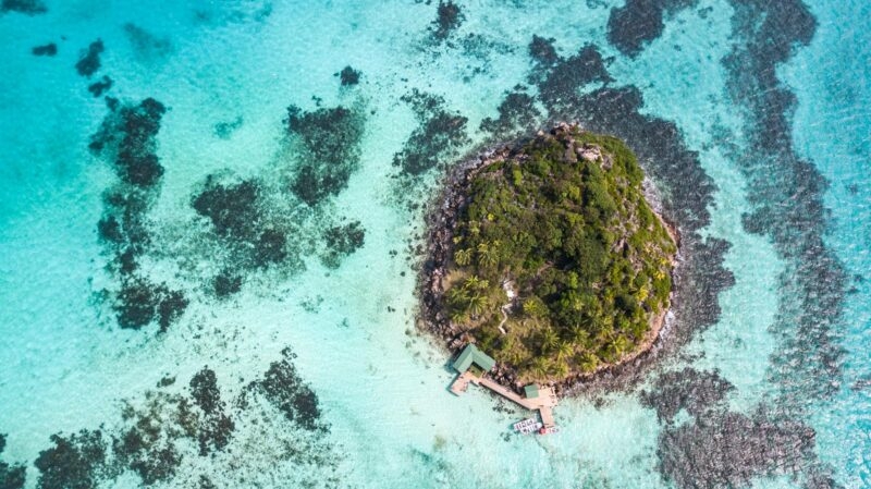An aerial, high-angle shot of a small, lush tropical island surrounded by clear, turquoise water and coral reefs, a perfect spot for Luxury Colombia vacations.