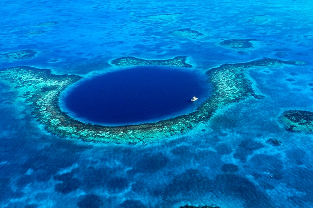 Aerial view of the Great Blue Hole, a large, deep blue, circular sinkhole surrounded by a shallow coral reef. Essential for luxury Belize tours.