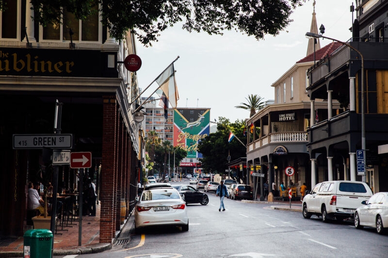 Luxury South African Tours - View of a city street with cars, pedestrians, and various shopfronts under a clear sky.