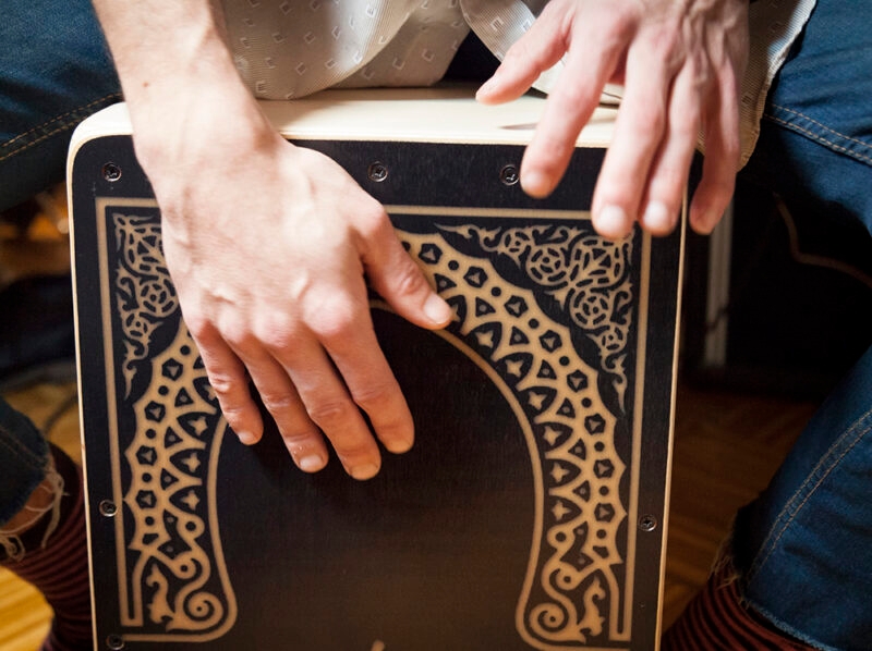 Close-up of a person's hands playing the top of a decorated wooden cajon drum, a sound of luxury Portugal vacations.