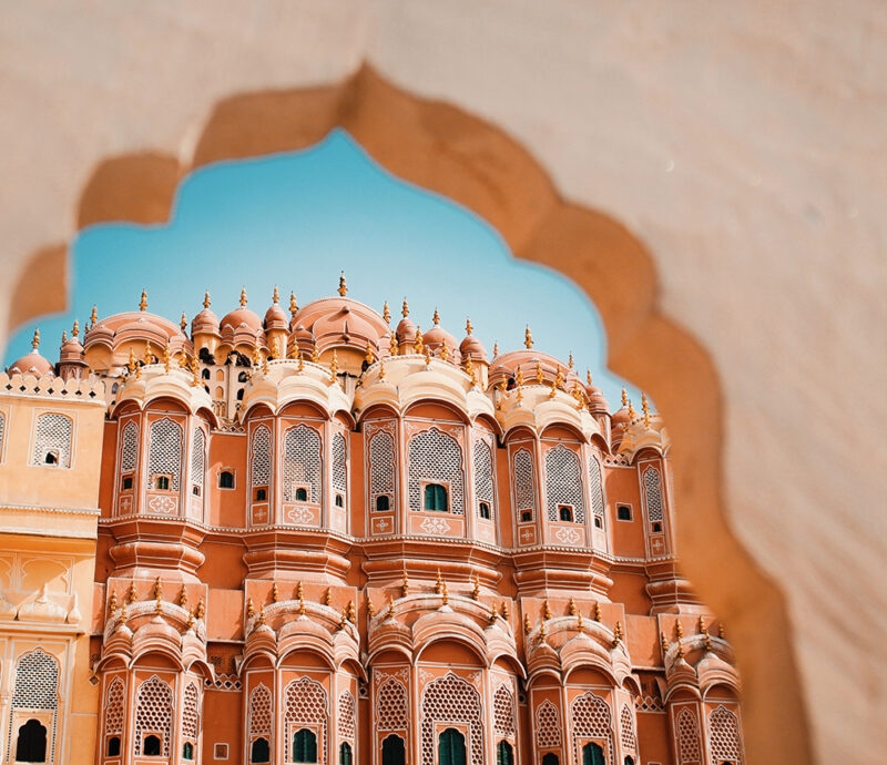 The pink and orange facade of the Hawa Mahal palace in Jaipur, seen through an arched doorway on luxury India tours.