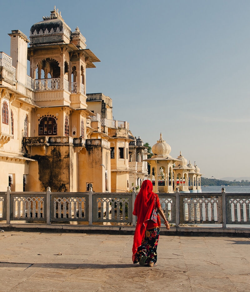 Woman in red sari stands on a terrace overlooking a lake and an ornate palace structure, on a luxury India tours.