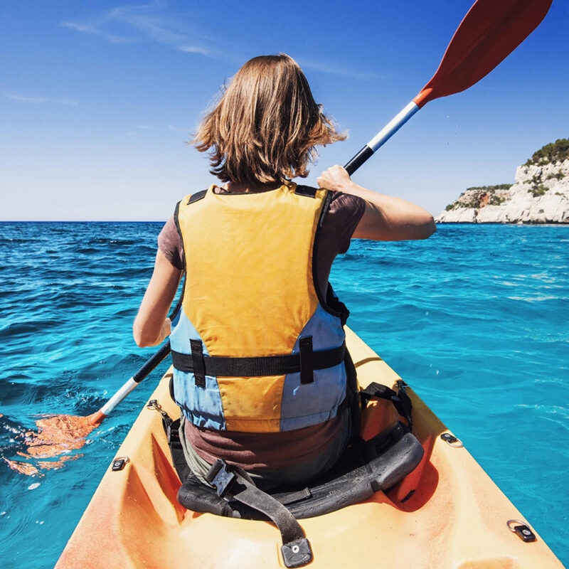 Person in a yellow life vest kayaking on blue water during luxury Italy family holidays.