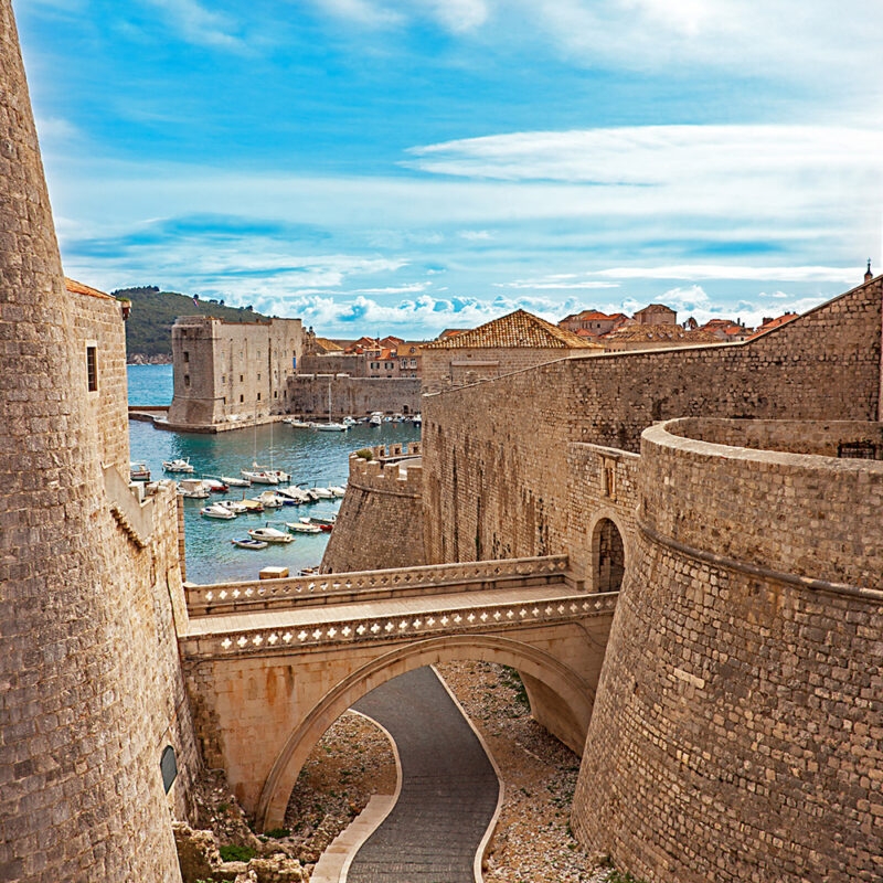 Medieval stone bridge and defensive walls of an old city harbor during luxury Croatia holidays.