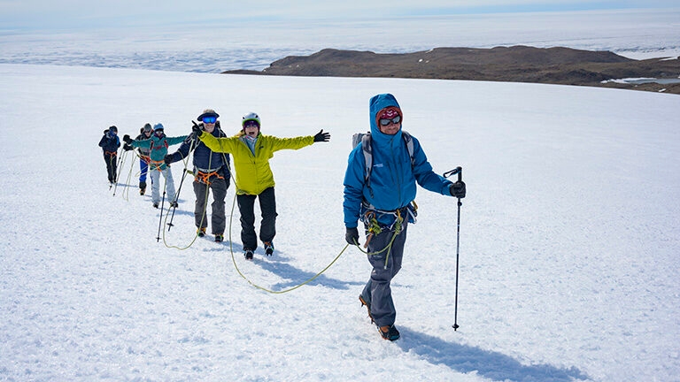A group of people roped together trekking across a vast glacier on Luxury Polar tours.
