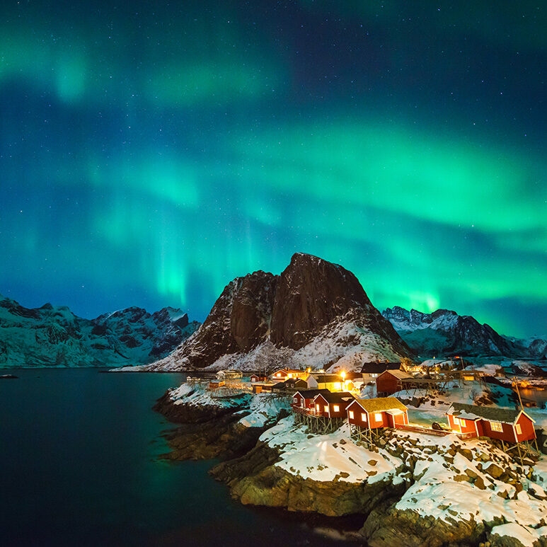 Green northern lights over a snowy village with red houses, a highlight of luxury Polar holidays.