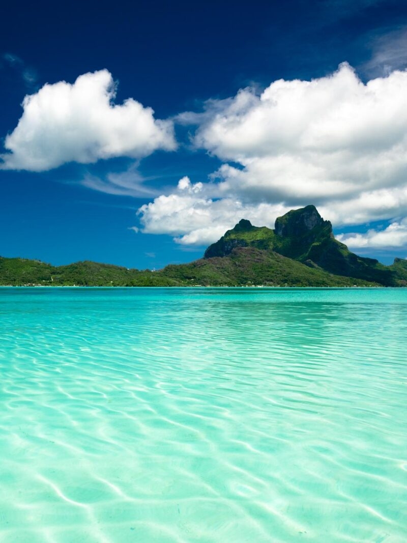 Volcanic mountain peak overlooking a clear turquoise lagoon during luxury South Pacific vacations.