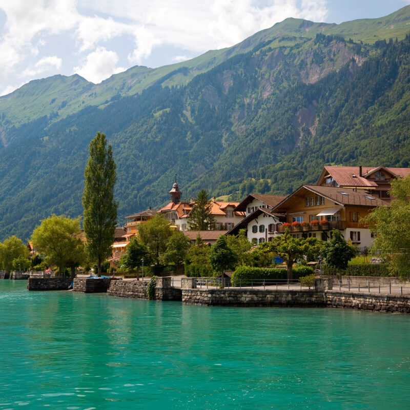 Lakeside village with traditional chalets nestled against steep green mountains during luxury Switzerland tours.