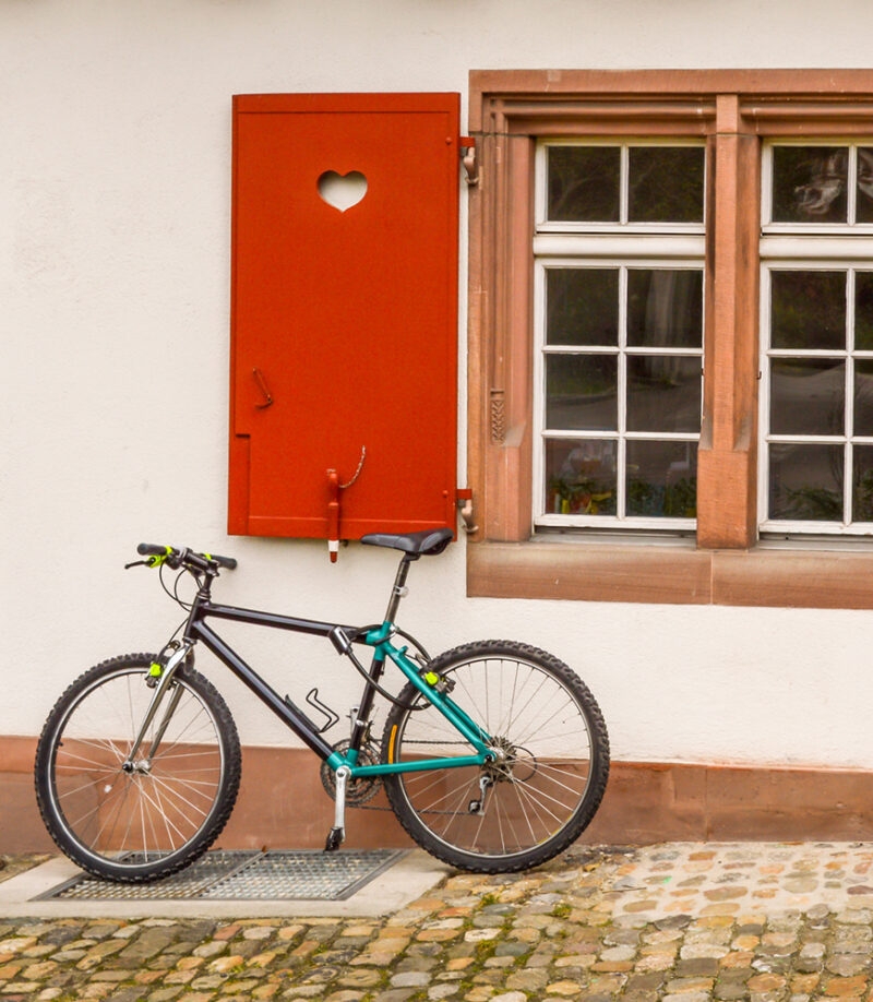 Bicycle parked against a building with a red wooden window shutter featuring a heart cutout on luxury Switzerland tours.