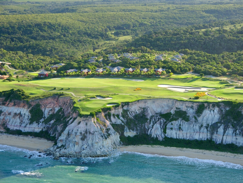 Aerial view of a coastal golf course built on white cliffs overlooking a beach and the ocean, surrounded by forest. luxury Brazil trips.